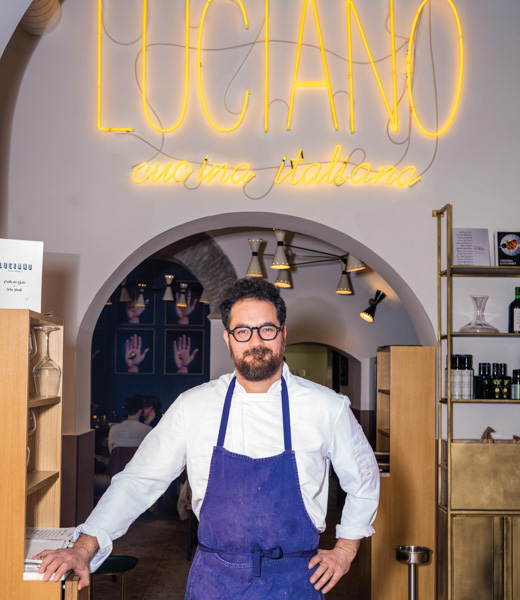 Luciano Monosilio underneath a neon sign bearing his restaurant's name.