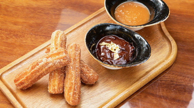 A pile of 4 churros served with chocolate and caramel dips