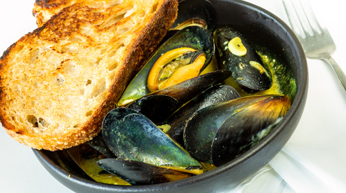 Bowl of mussels with a side of bread.